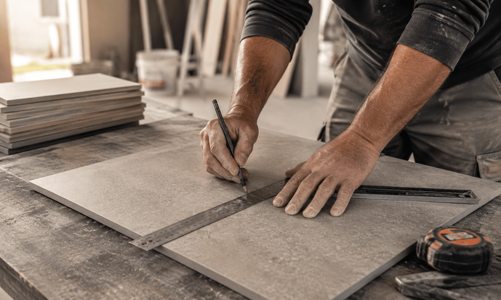 Artisan carreleur pr&eacute;parant et mesurant un carreau avant la pose